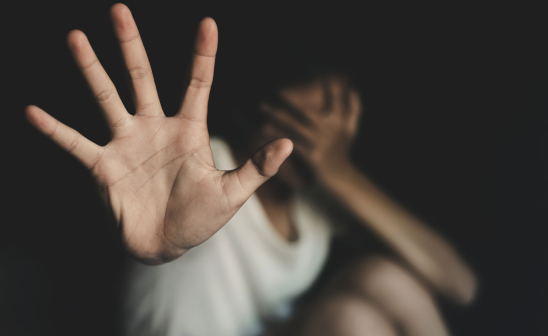 Persona alzando la mano en señal de detener mientras se cubre el rostro, simbolizando miedo o rechazo. Representación de situaciones de violencia o abuso. - w-100